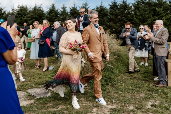 Bride and groom walk from ceremony guests clapping in background