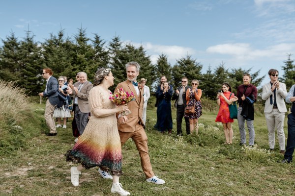 Bride and groom walk from ceremony guests clapping in background