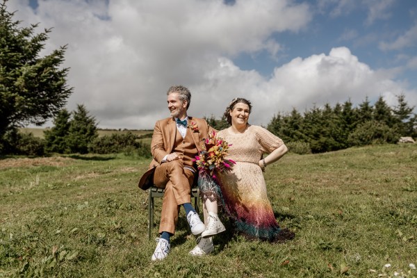 Bride groom sit on chairs in the grass countryside skyline