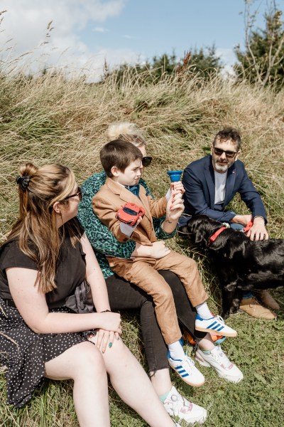 Family members and little boy sit in the grass wearing sunglasses in the sun