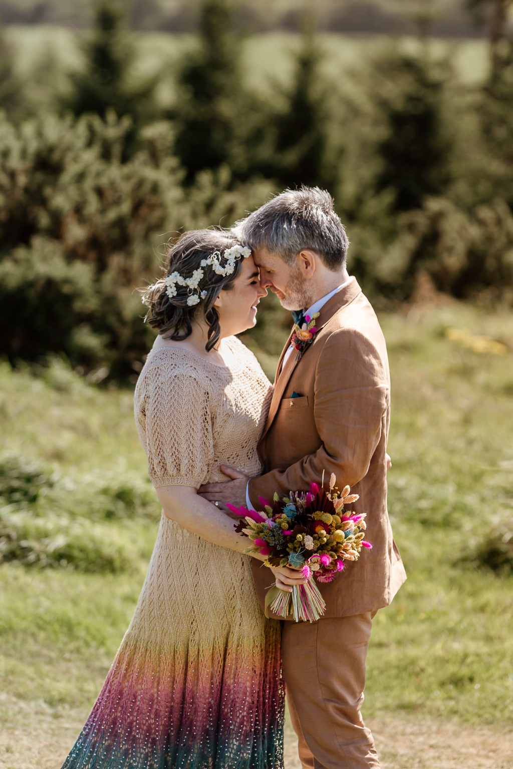 Bride and groom touch foreheads holding each other on the grass