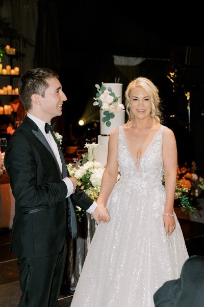 Bride and groom stand in front of the white wedding cake