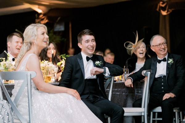 Groom and bride sit and laugh during speeches