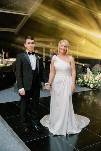 Bride and groom stand holding hands