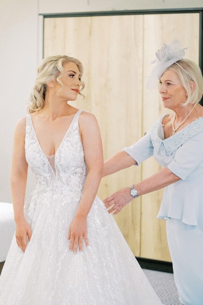 Bride gets help from mother zipping up back of dress