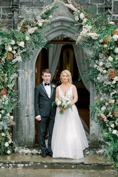 Bride and groom pose outside of church flower bed