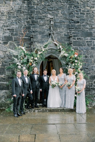 Bride groom bridesmaids and groomsmen pose outside of church flower bed