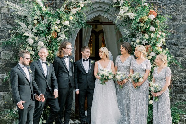 Bride groom bridesmaids and groomsmen pose outside of church flower bed