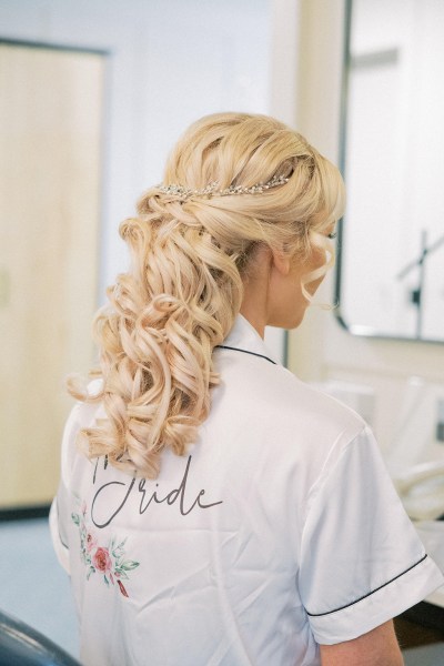 Bride is getting her hair styled by hairstylist from behind blonde waves