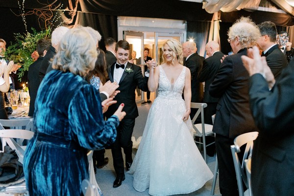 Bride and groom hold hands as guests clap