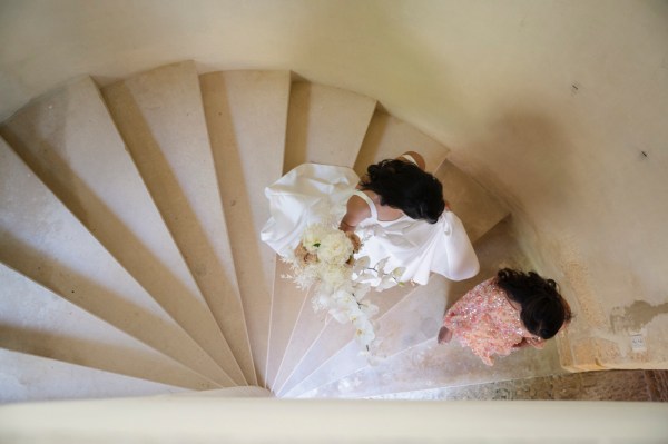 Bride walks down venue staircase heading towards venue flowers in hand