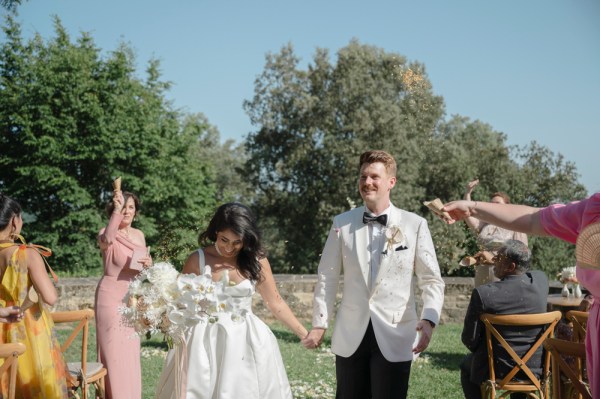 Bride and groom exit ceremony guests clapping she holds bouquet