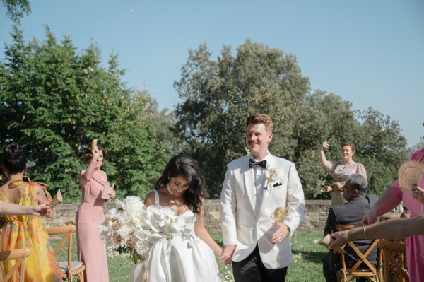 Bride and groom exit ceremony guests clapping she holds bouquet