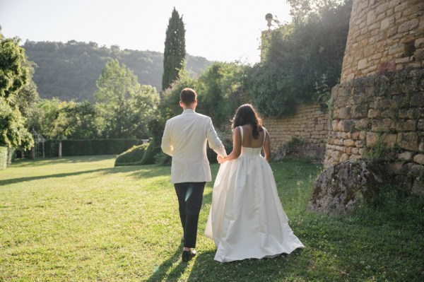 Bride and groom walk hand in hand on the grass sunshine