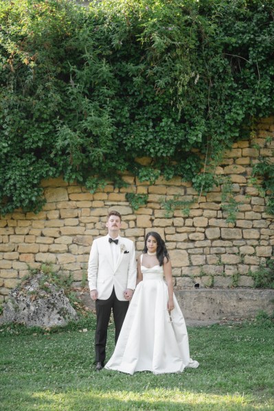 Couple stand on the grass castle venue in background bricked wall in background