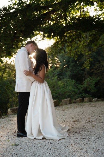 Bride and groom hold each other on pathway to forest they look at each other and go in for a kiss