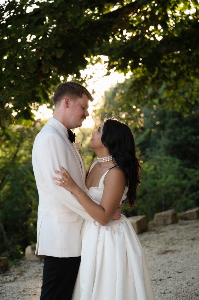 Bride and groom hold each other on pathway to forest they look at each other