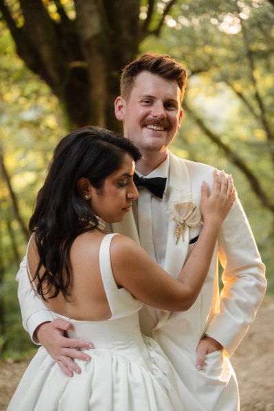 Bride and groom hold each other groom smiles in forest