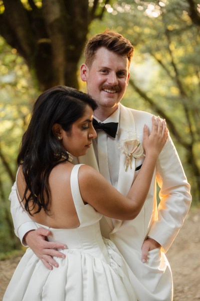 Bride and groom hold each other groom smiles in forest