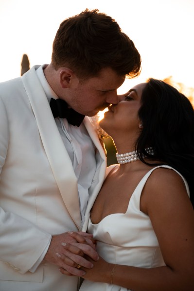 Bride and groom laugh as they hold each other sunset in background going in for a kiss