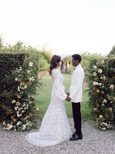 Bride and groom holding hands between hedges in garden