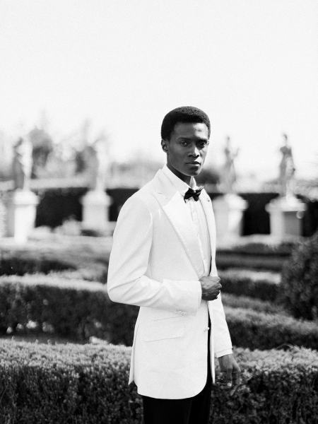 Groom stands in maze garden on his own on grass black and white