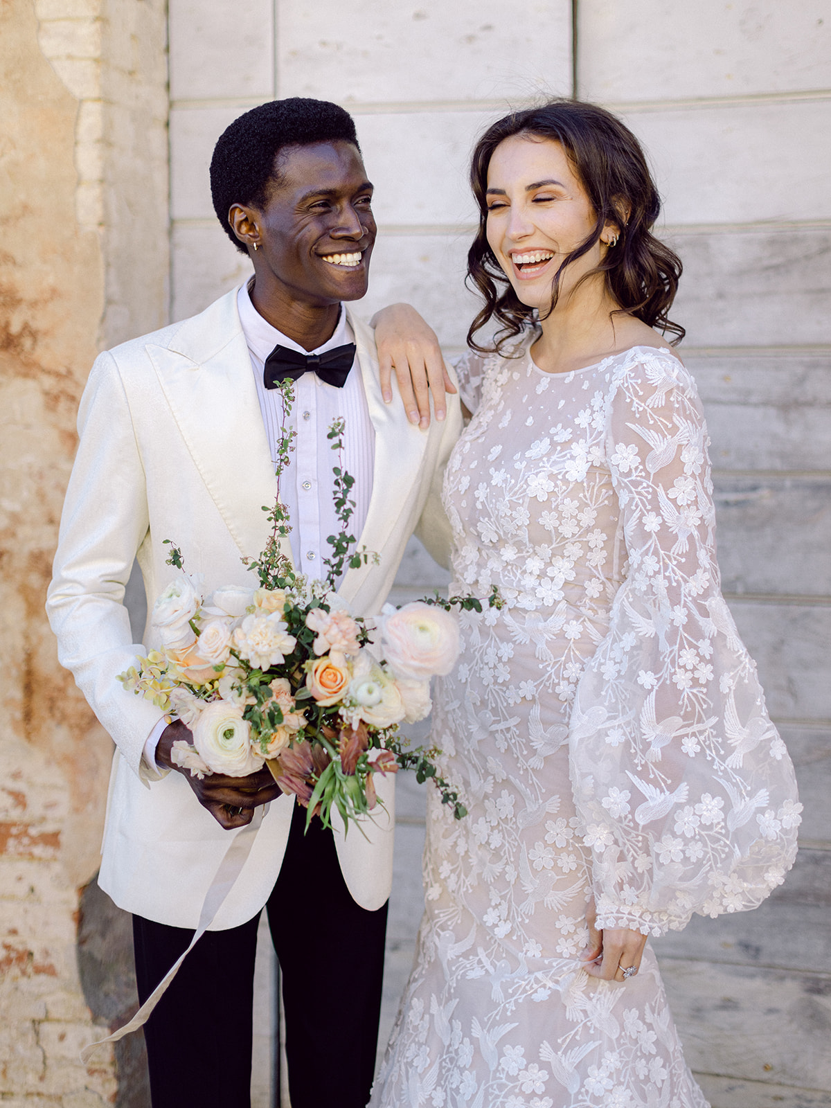 Bride has hand on grooms shoulder she holds bouquet as they smile