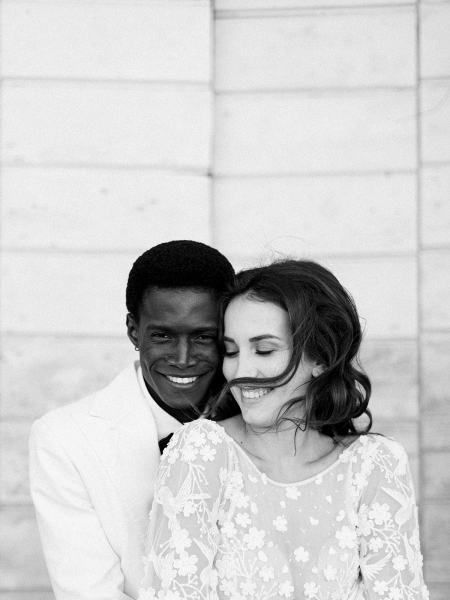 Groom hugs bride from behind she holds bouquet smiling black and white