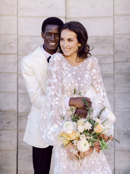 Groom hugs bride from behind she holds bouquet smiling