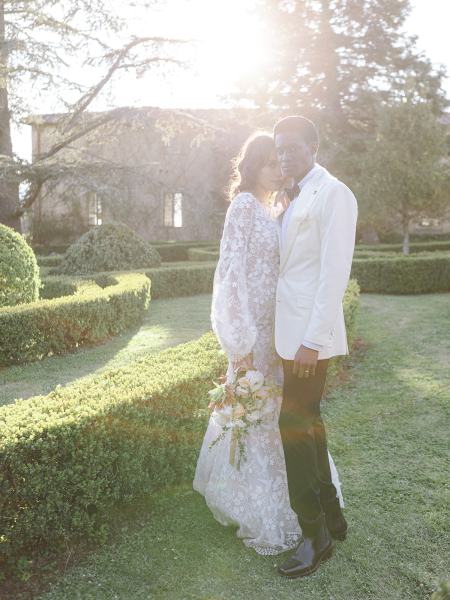 Bride stands with bouquet in hand with groom on the grass in garden