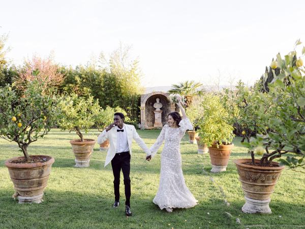 Bride and groom hold hands in garden and walk along the grass