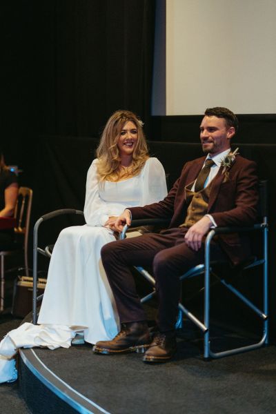 Bride and groom smile at top of platform cinema room screen in background stage