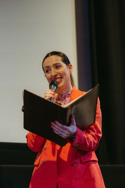 Celebrant smiles as she reads from booklet speaks into microphone