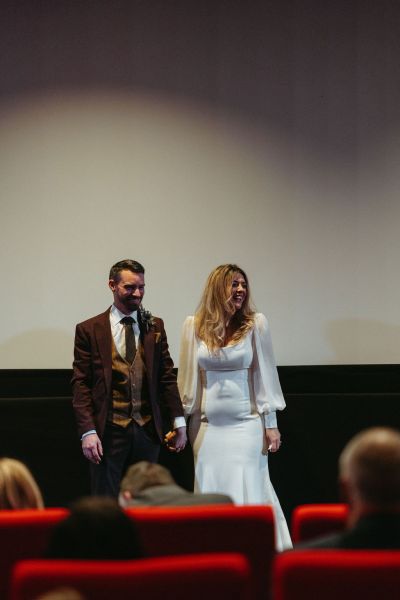 Bride and groom stand at top of cinema room screen in background