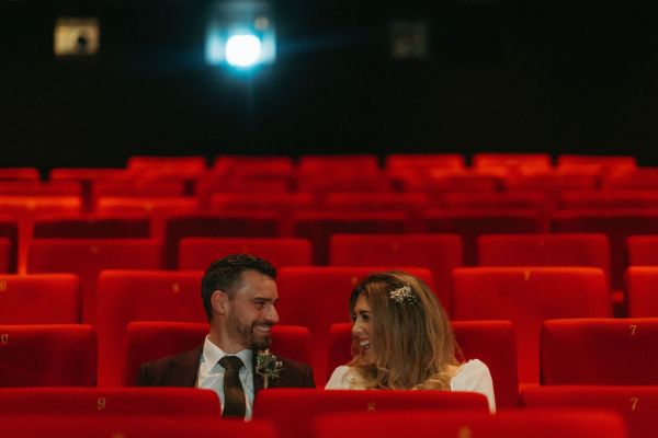 Bride and groom sit in audience red chairs in cinema room