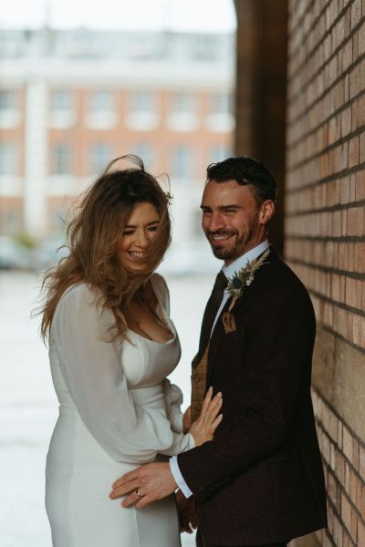 Bride and groom standing against brick wall at Queen's University archway