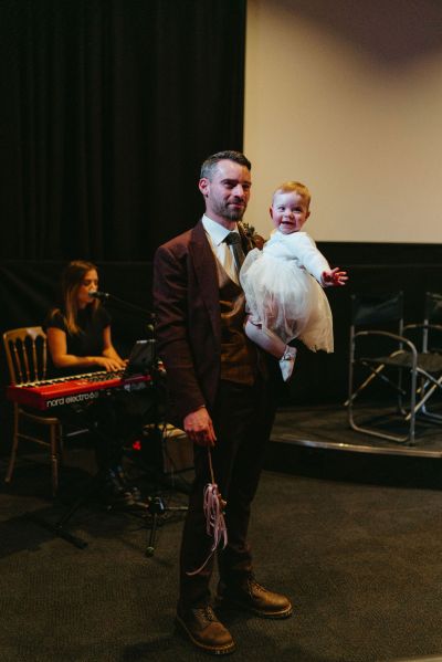 Groom carries holds his daughter baby girl in little white dress