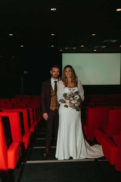 Bride and groom pose on the cinema aisle together