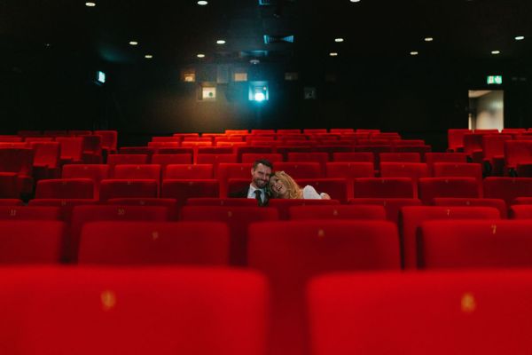 Bride and groom seated in cinema on red chairs