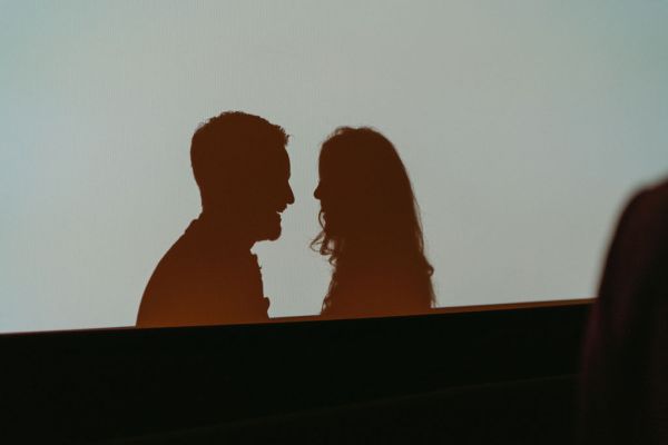 Shadow reflection of bride and groom against cinema screen touching heads