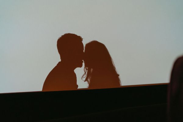 Shadow reflection of bride and groom against cinema screen touching heads