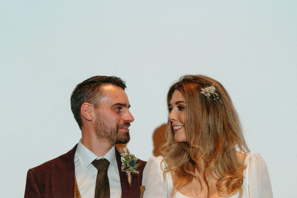 Bride and groom look at each other standing against white cinema screen