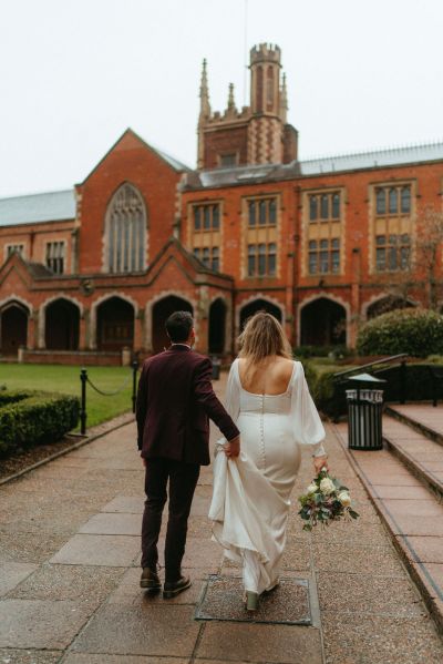 Bride and groom walking outside wedding venue grass area from behind