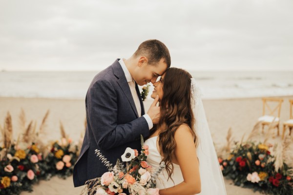 Bride and groom kiss in front of ocean view setting holding bouquet