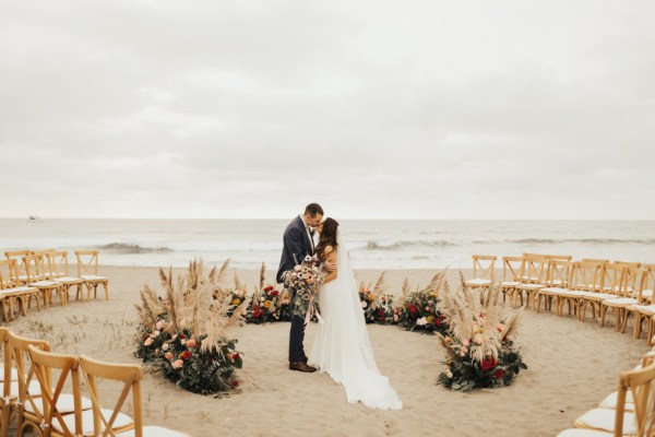 Bride and groom kiss in front of ocean view setting holding bouquet