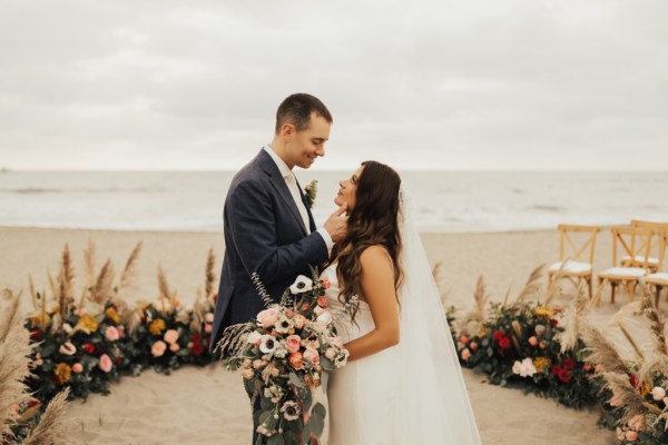 Bride and groom kiss in front of ocean view setting holding bouquet