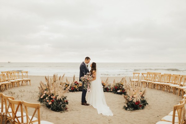 Bride and groom kiss in front of ocean view setting holding bouquet