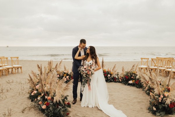 Bride has hand on grooms cheek beach setting