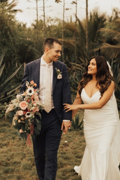 Bride and groom standing on grass walking in front of palm trees beach setting they look at each other