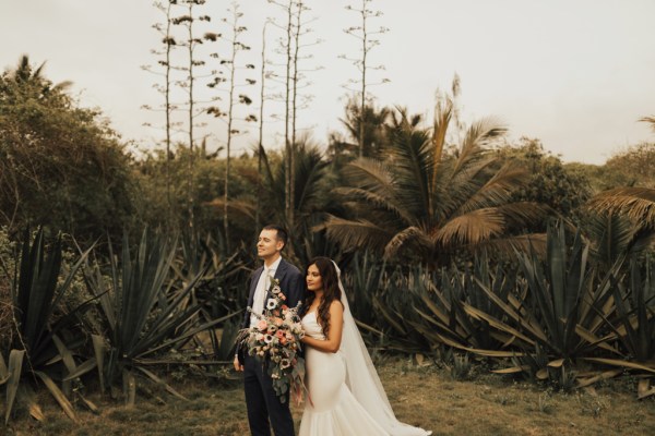 Bride and groom standing on grass walking in front of palm trees beach setting